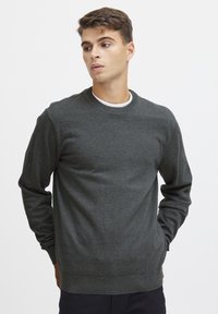 Suéter gris oscuro hecho de tela suave, con cuello redondo y puños y dobladillo acanalados para un ajuste estructurado. Diseño minimalista sin patrones.