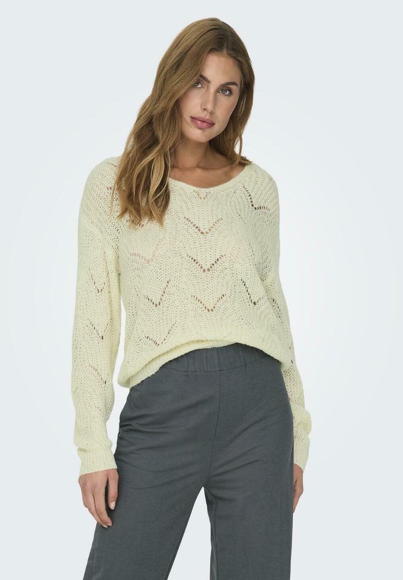 Maglione lavorato a maglia di un giallo chiaro con un motivo a zig zag, collo rotondo e maniche lunghe, abbinato a pantaloni grigi.