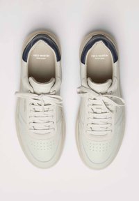 Zapatillas de cuero gris claro con acentos en azul marino, puntera redonda, detalles perforados, cordones planos y un logo sutil en la plantilla.