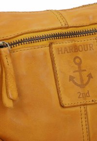 Borsa in pelle gialla con chiusura a zip e design a rilievo di un'ancora. Superficie testurizzata con dettagli di cucitura a contrasto.