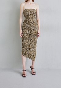 Robe midi sans bretelles en imprimé léopard avec texture plissée, ourlet asymétrique et coupe ajustée. Modèle portant des escarpins noirs à lanières.