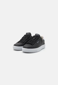 Czarne skórzane sneakersy z niskim profilem, okrągłym czubkiem, białą gumową podeszwą i czarnymi sznurowadłami. Uzupełnione białą wstawką na pięcie.