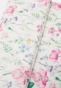 Překládaná bílá látka s barevným květinovým vzorem, který zahrnuje růžové, fialové a modré květiny, a malý detail zlatého kovového loga.