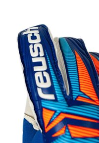 Close-up of a blue goalkeeper glove with orange and light blue geometric patterns and the brand name "reusch" in white letters.