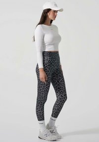 Crash legging s printom tigra u crnoj i sivoj boji u kombinaciji s bijelim dugim rukavima crop topom i bijelom kapicom. Imaju teksturiranu tkaninu i elastičnu rezbariju.
