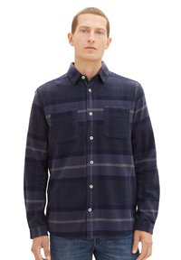 Granatowa koszula w kratę z białymi i szarymi paskami, zapinana na guziki z przodu, z dwoma kieszeniami na piersi oraz miękką teksturowaną tkaniną. Długie rękawy z mankietami na guziki.