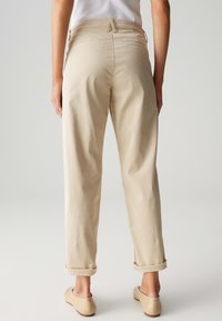 Beige, hochtaillierte Hose mit lockerem Schnitt, aufgeschlagenen Säumen und Gesäßtaschen. Glattes Material mit minimalen Nähten.