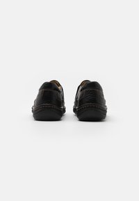 Schwarze Lederschuhe mit strukturierter Oberfläche und Stichdetails. Abgerundete Form und gepolsterte Sohle. Die Rückansicht zeigt das klare Design und die Konstruktion.