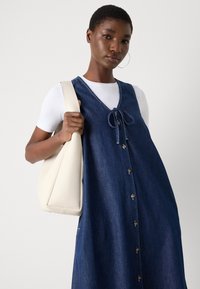 Denimkjole med V-hals, knyte-detall og knappelukking. Har en løs passform og er kombinert med en veske i kremfarge.