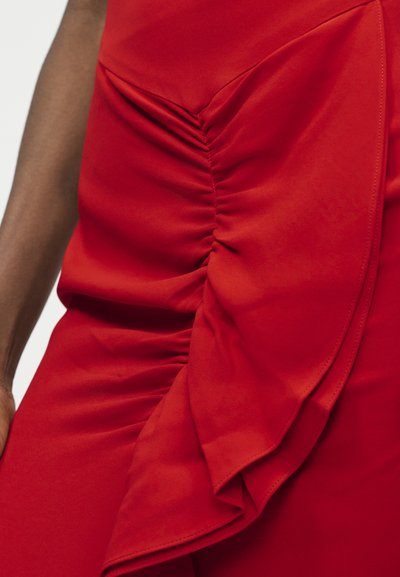 Primer plano de un vestido rojo fruncido con un detalle de volantes en capas en un lado, llevado por una persona de piel oscura.