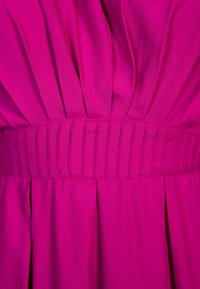 Tissu rose vif avec des plis verticaux et une large ceinture texturée au centre.