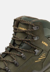 Grüner Wanderschuh aus strukturiertem Wildleder und Netzmaterialien. Merkmale sind kontrastierende gelbe und braune Schnürsenkel, Metallösen und Logo-Akzente.