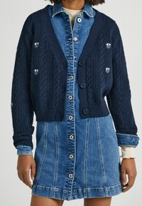 Navy cable-knit cardigan with short sleeves, button closure, and decorative accents paired with a denim shirt dress featuring a front button placket.