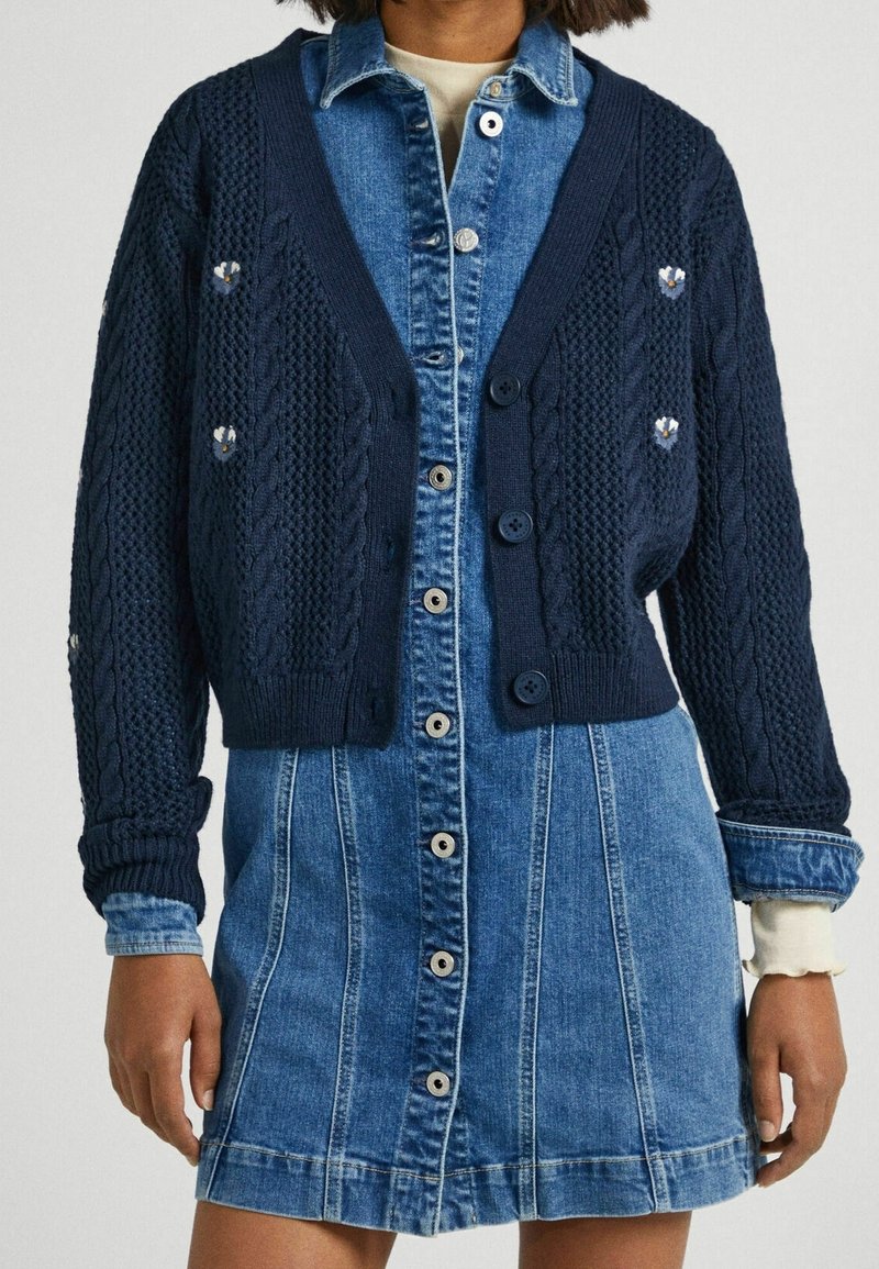Navy cable-knit cardigan with short sleeves, button closure, and decorative accents paired with a denim shirt dress featuring a front button placket.