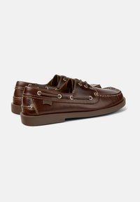 Zapatos de barco de cuero marrón con cordones, con un perfil bajo, superficie texturada, detalles de costura y suela de goma con un ligero tacón.
