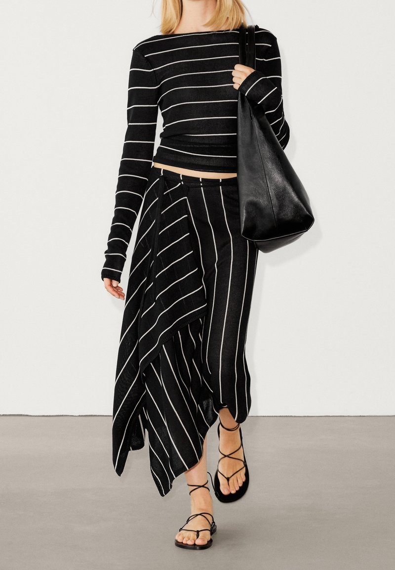 Zwart-wit gestreepte lange mouwen top en een asymmetrische rok, gecombineerd met platte zwarte sandalen en een grote zwarte tas. Zachte, vloeiende textuur.
