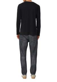 Czarna koszula z długim rękawem w połączeniu z wyblakłymi szarymi jeansami o luźnym kroju i subtelnymi detalami na tylnych kieszeniach. Całość uzupełniają jasne buty.