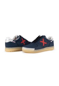 Zapatillas de lona de color navy con un logo rojo en forma de "X", cordones negros, detalles en blanco y una suela de goma translúcida; parte superior de tela texturizada y detalles cosidos.