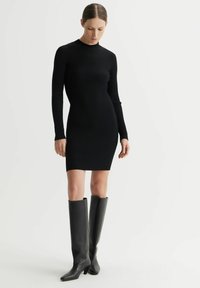 Czarna, prążkowana, dzianinowa sukienka z długim rękawem, prosta, do kolan. Para wysokich czarnych skórzanych botków z kwadratowym noskiem i słupkowym obcasem.