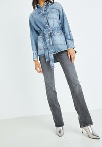 Jeansjacka med bälte i midjan, med två bröstfickor och en ljusblå tvätt, tillsammans med smalpassande grå jeans och silverfärgade spetsiga klackar.