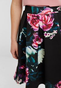 Gonna floreale con vivaci fiori rosa e bianchi su uno sfondo nero, caratterizzata da pieghe e una cintura liscia.