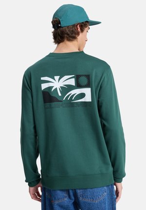Sudadera verde con un estampado gráfico de palmeras, montañas y sol. Está hecha de una tela suave con puños y dobladillo acanalados.