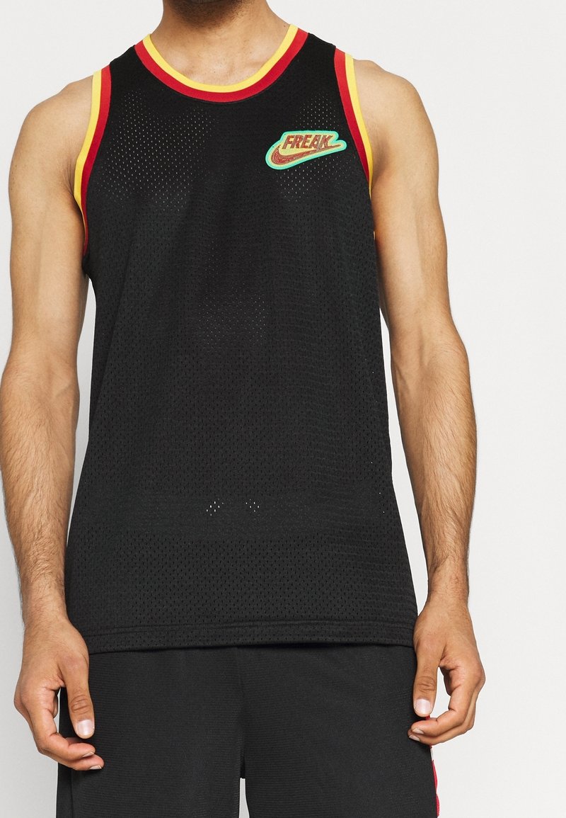 Homme portant un maillot de sport noir sans manches en mesh avec des bordures rouges et jaunes et un logo coloré "FREAK" sur la poitrine.
