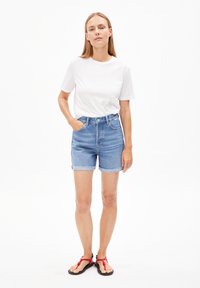 Hoge taille denim shorts met een lichtblauwe wassing, rafelige zoom en vijf zakken, gecombineerd met een effen wit katoenen t-shirt en zwarte sandalen.