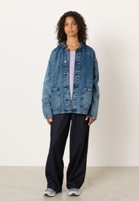 Jeans jakna z svetlim in temnim pranjem, gumbi spredaj in dvema sprednjima žepoma, kombinirana s hlačami s tankimi črtami in sivimi supergami.