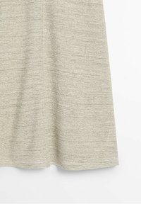 Panneau en tissu tricoté beige texturé avec une couture verticale visible, probablement partie d'un vêtement, présenté sur fond blanc.