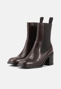 Botas de tornozelo de couro castanho-escuro com painéis elásticos laterais, bico redondo e um salto bloco. Textura suave com detalhes de costura mínimos.