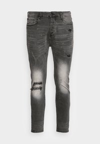 Černé džíny z denimu se zařezaným designem, vybavené několika trhlinami a vyblednutím pro postarší vzhled. Úzce padnoucí s zúženou nohavicí.