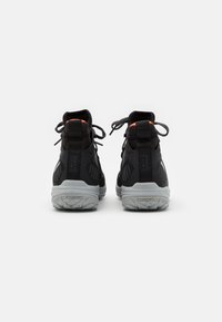 Scarpe da trekking nere con design alto, dettagli riflettenti e suole in gomma grigia. Presentano una superficie testurizzata e lacci regolabili.