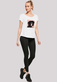 White short-sleeve t-shirt featuring a graphic print of a figure with dark hair in black and pink tones, paired with black leggings and sneakers.