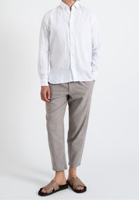 Biała lniana koszula na guziki, jasnoszare lniane spodnie oraz brązowe wsuwane sandały z wycięciami, na neutralnym tle.