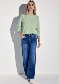 Ljusgrön, långärmad tröja i kombination med vida blåjeans. Uppsättningen har en avslappnad passform och framfickor. Vita skor kompletterar looken.