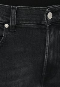 Blugi negri din denim, cu design clasic cu cinci buzunare, accesorii argintii și un finisaj texturat al țesăturii. Talie cu închidere cu nasture metalic.