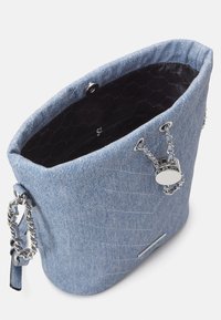 Sac seau en denim bleu avec une texture matelassée, des anses en chaîne argentée et un intérieur noir doté d'une poche zippée et d'une fermeture à bouton-pression.