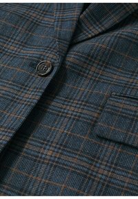 Tissu à carreaux bleu foncé et marron avec un tissage texturé, montrant un gros plan d'un bouton noir à quatre trous et d'un rabat de poche sur une veste.