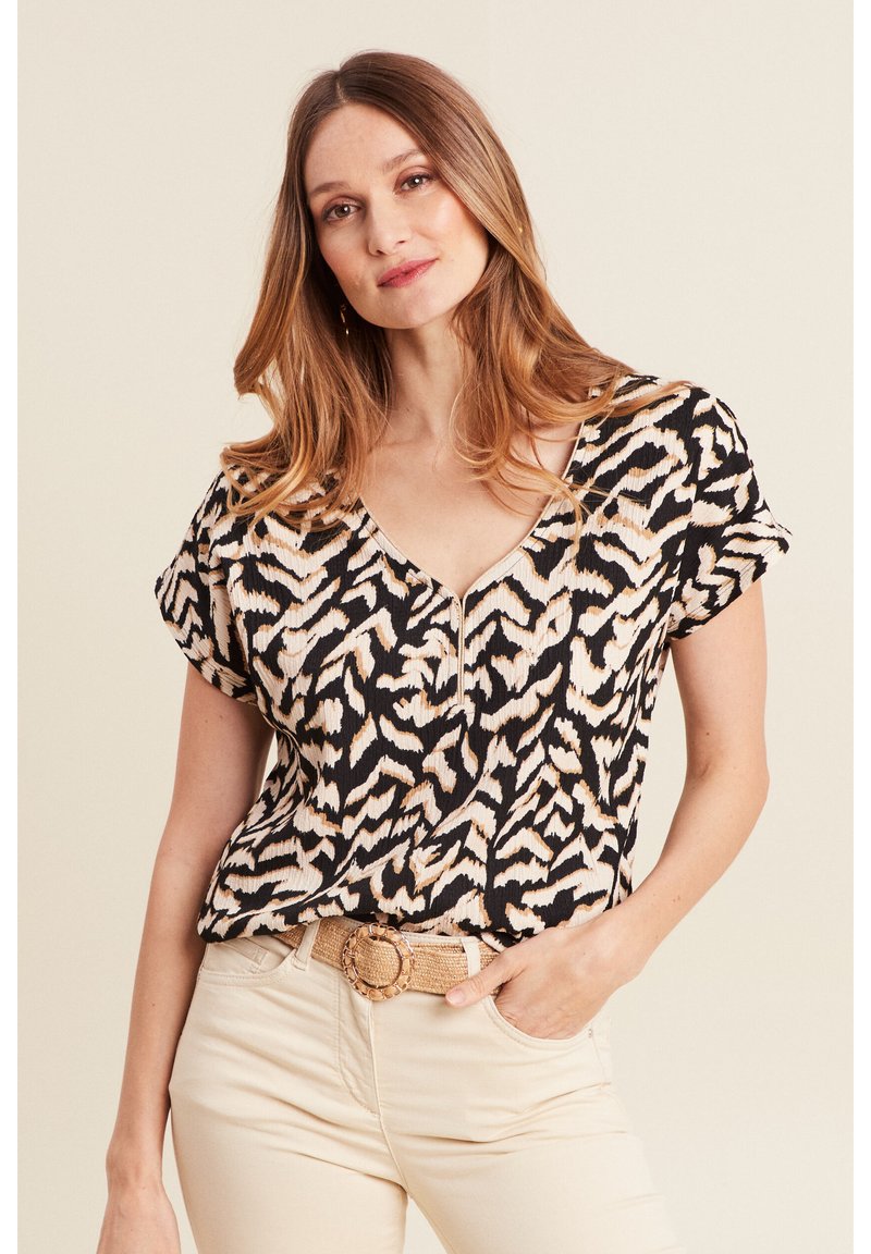 Top nero con stampa animale beige chiaro e maniche corte, dotato di scollatura a V e pieghe sottili, abbinato a pantaloni beige e una cintura intrecciata.