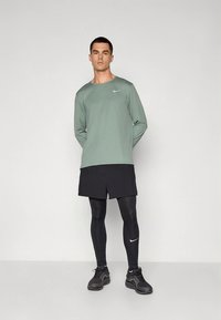 Nike helikätega särk helerohelises toonis, mustad spordipüksid ja mustad retuusid. Särgil ja kingadel on väike valge logo.