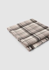 Złożony koc w kratę w odcieniach beżu i kremu z ciemnoszarymi akcentami. Posiada frędzlowe krawędzie oraz miękką, teksturowaną powierzchnię.