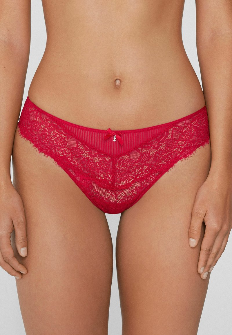 Culotte de bikini en dentelle rouge avec des motifs floraux, un accent de nœud au centre avant et des bords doux et effilochés pour une texture supplémentaire.