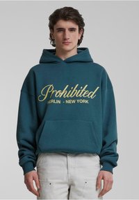 Teal hættebluse med guldskrift, der står "Prohibited BERLIN - NEW YORK," med kengurulomme og ribbede håndled, lavet af blødt stof.
