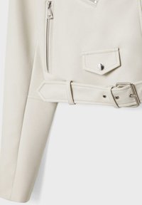 Nahaufnahme eines weißen Lederjackenärmel mit einem silbernen Reißverschluss, einer Druckknopftasche und einem passenden Gürtel mit silberner Schnalle.