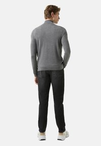 Grauer Pullover mit schmaler Passform, gerippten Bündchen und Saum. Gesehen von hinten, getragen zu dunklen Jeans und Turnschuhen, wobei der Halsausschnitt hervorgehoben wird.