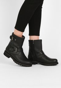Bottines en cuir noir avec fermeture éclair sur le côté, accents de boucles et semelles texturées. Fini lisse avec un design robuste.
