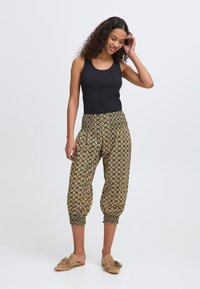 Débardeur noir côtelé associé à un pantalon ample à motifs, doré et noir, avec des poignets élastiques et une taille confortable.