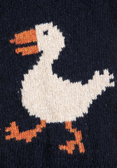 Strickstoff mit einem weißen Entenmotiv, das einen orangefarbenen Schnabel und Füße auf einem marineblauen Hintergrund zeigt. Die Textur ist weich und das Garn wirkt leicht flauschig.