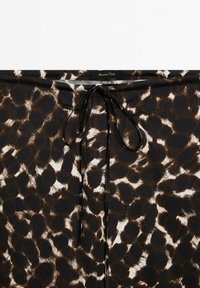 Tessuto con stampa animale nera e marrone, con una superficie liscia, caratterizzato da un dettaglio con nodo frontale e un'etichetta al centro superiore.
